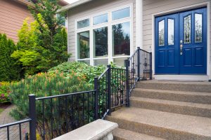The front entryway of a home with stairs, a black railing, and blue entry doors.