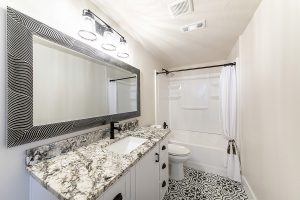 A modern bathroom with a new acrylic bathtub, large vanity mirror, and a white marble counter top.